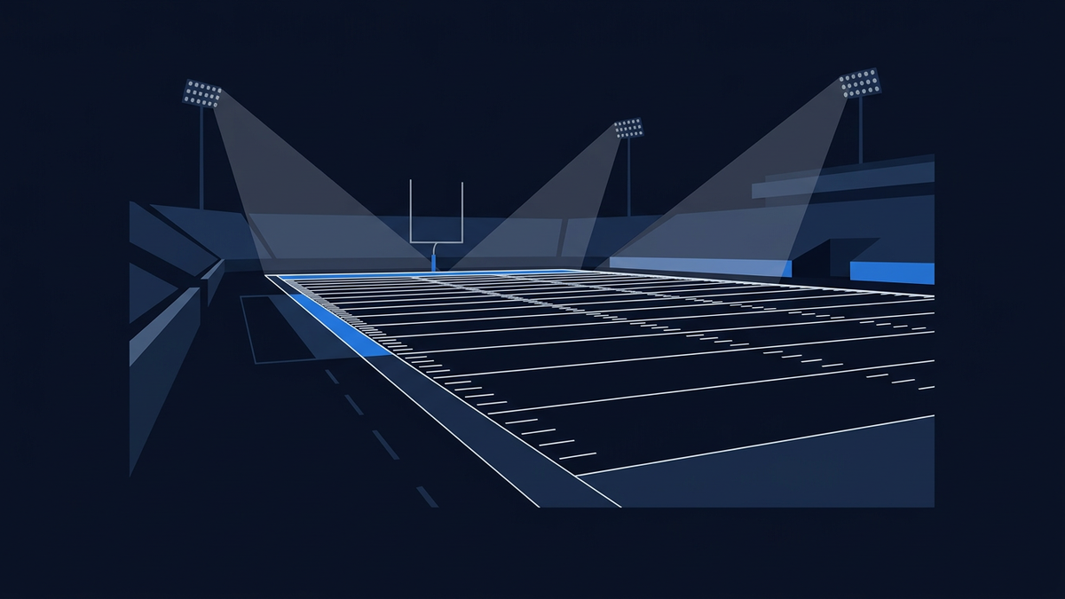 An empty American football field at night seen from a low sideline angle in deep navy, white yard lines and hash marks receding in perspective, a bare goalpost in the distance, and floodlight pylons casting pale cones of light over empty stands