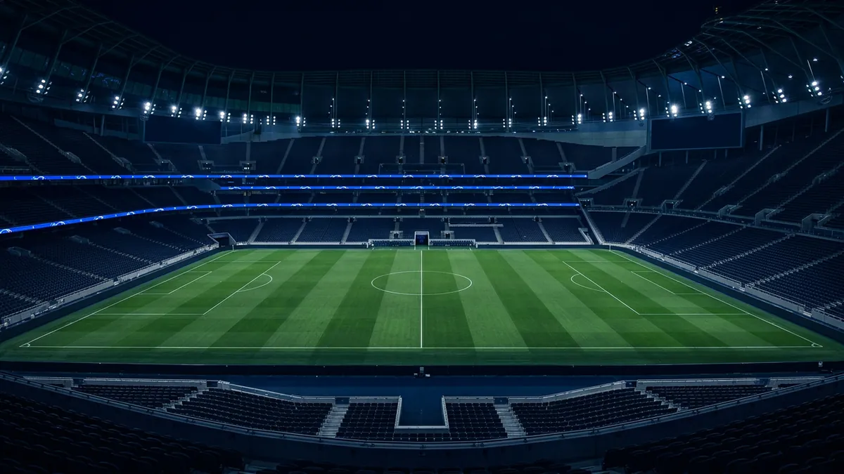 An empty football stadium at night, photographed from a low end-stand angle, showing a floodlit green pitch with white markings, dark navy seating tiers, and blue LED ribbon boards ringing the stands.