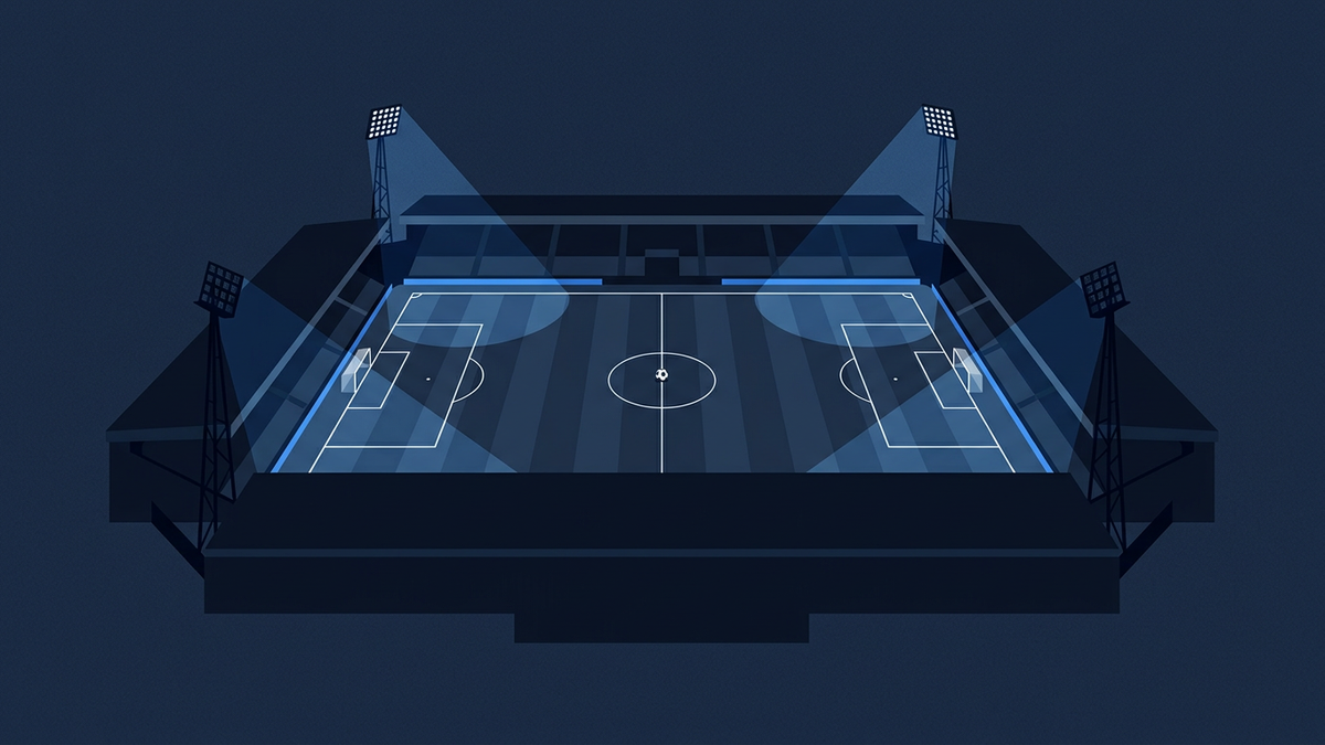 An empty football stadium seen from above one corner in deep navy, the pitch marked out with a centre circle and penalty areas, four floodlight pylons casting pale cones of light, and a single ball on the centre spot
