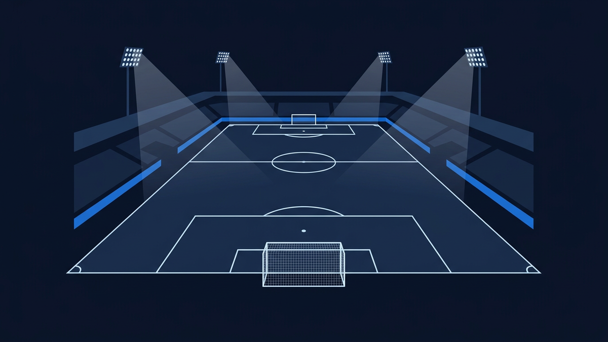 An empty floodlit football pitch at night in deep navy, seen from a low angle behind one goal, with white penalty areas, centre circle and halfway line receding in perspective, a netted goal frame in the foreground and blank blue hoardings in front of empty stands